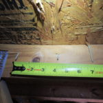 Photo of a tape measure extended across a roof truss with several exposed nails.