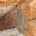 image of a metal hurricane tie securing a wooden roof truss to the wall.